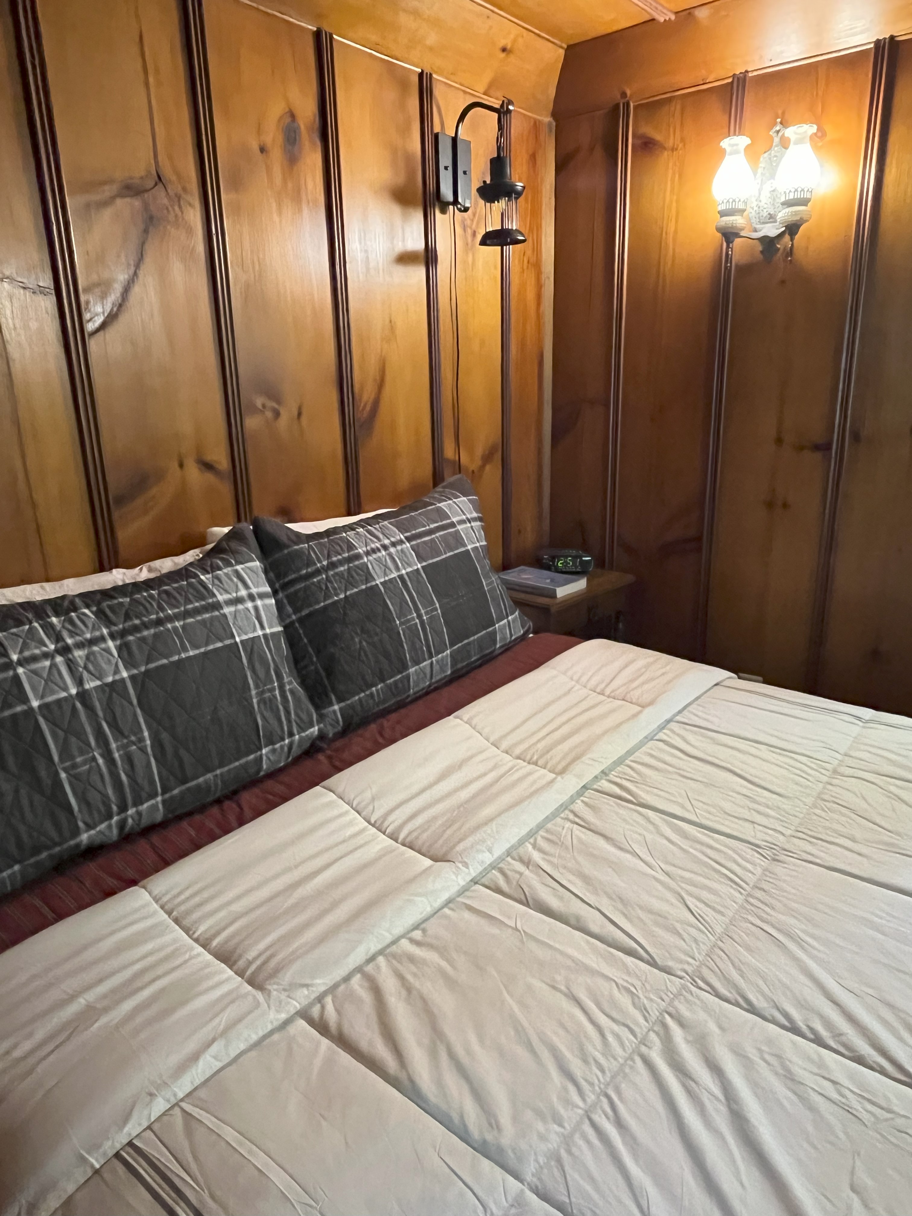 Queen bedroom with knotty pine walls, plaid pillows, and wall sconce lamps